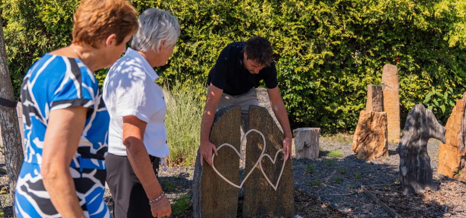 Adviseur van Hutting Natuursteen toont een hartornament aan twee klanten in de monumententuin