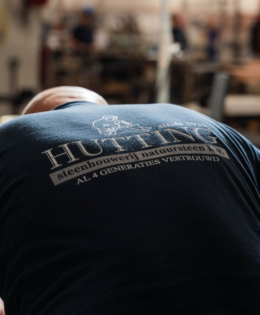Vakman in de werkplaats met het Hutting-logo op zijn rug: steenhouwerij natuursteen, al 4 generaties vertrouwd