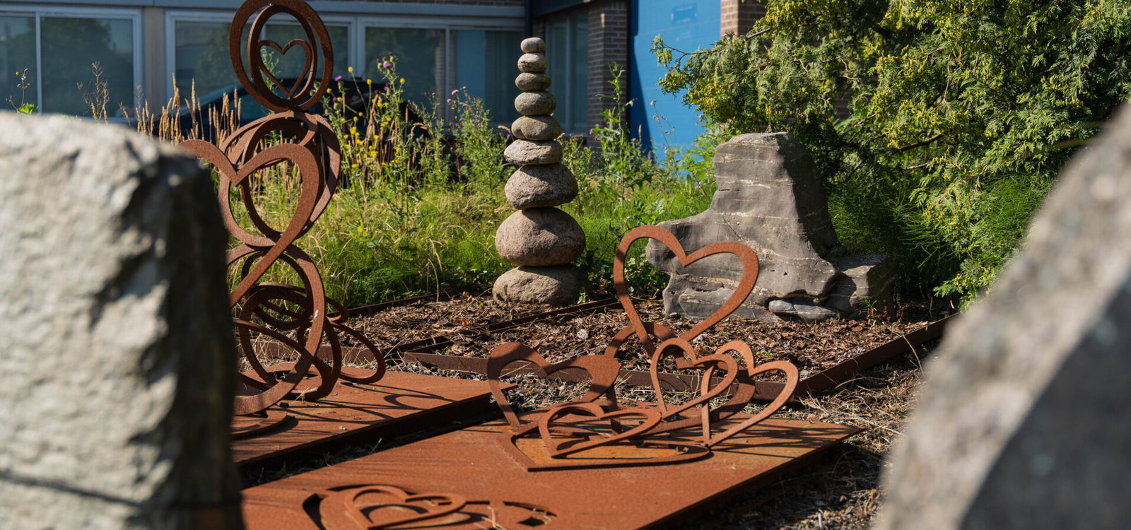 Cortenstalen ornamenten en gestapelde stenen bij een grafmonument